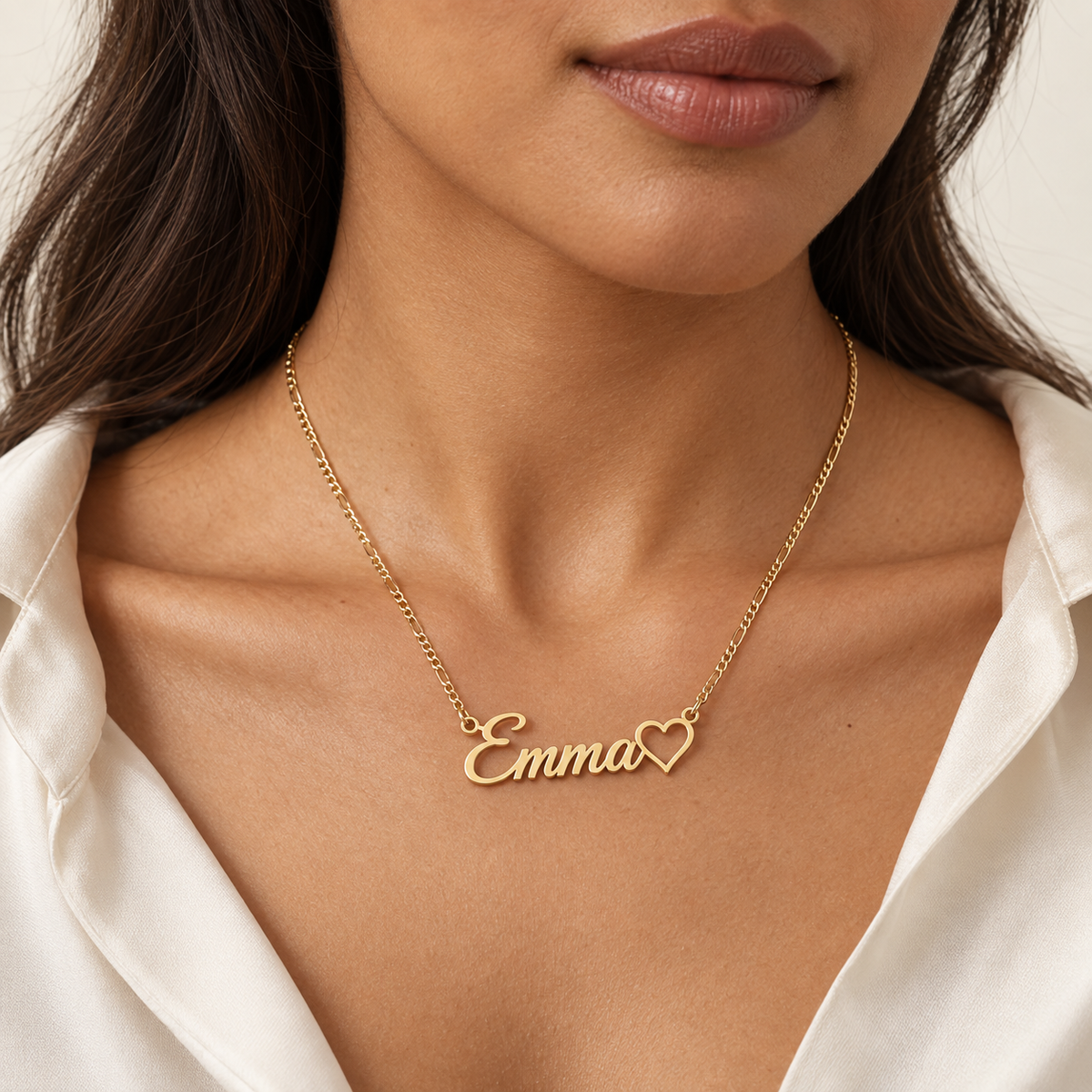 Woman wearing a gold personalized name necklace with heart detail and ivory blouse