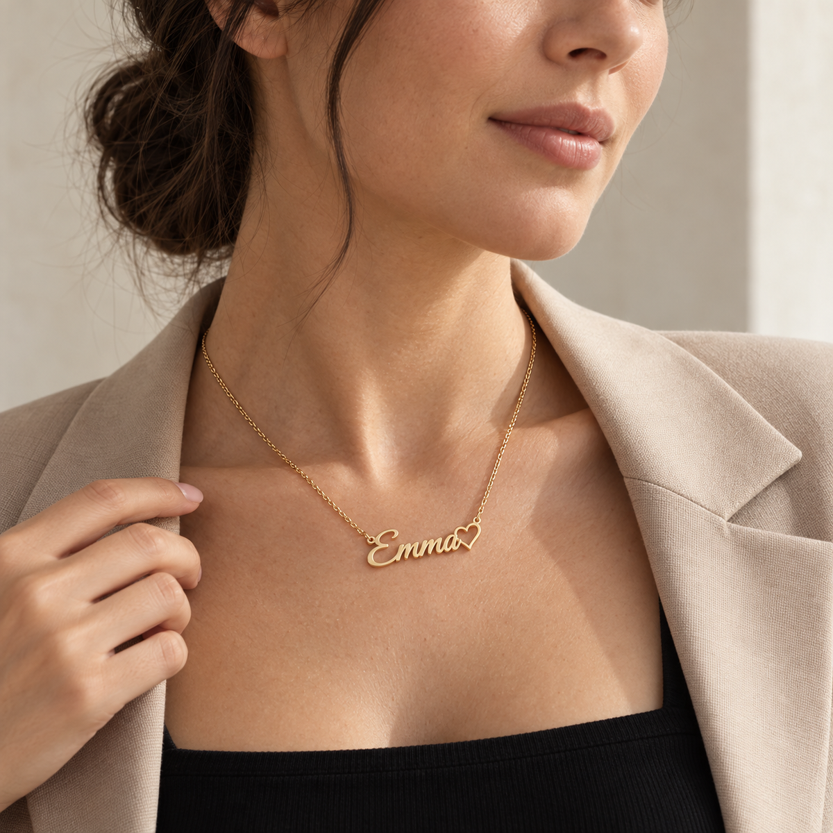 Woman wearing a custom gold script name necklace with a beige blazer and black top