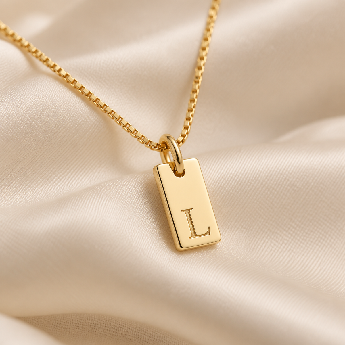 Close-up of the fine box chain and jump ring on a petite gold initial pendant necklace